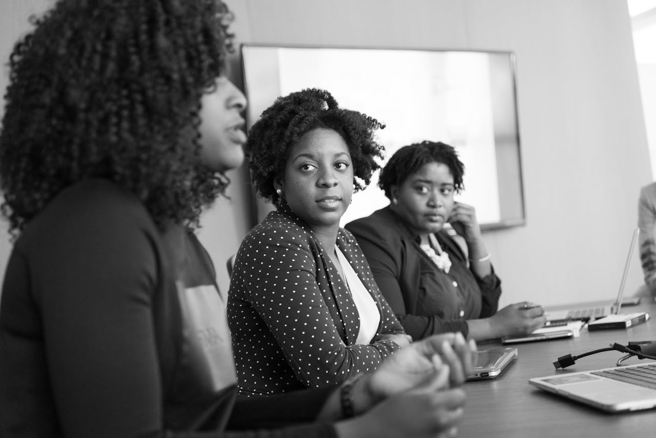 Three black women engaged in a serious discussion at an office meeting.