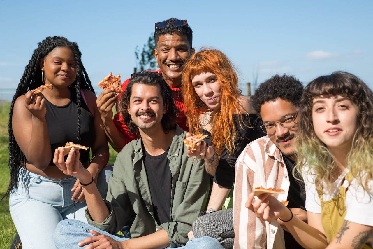 Group of friends having a fun picnic with pizza under a sunny blue sky in Portugal.