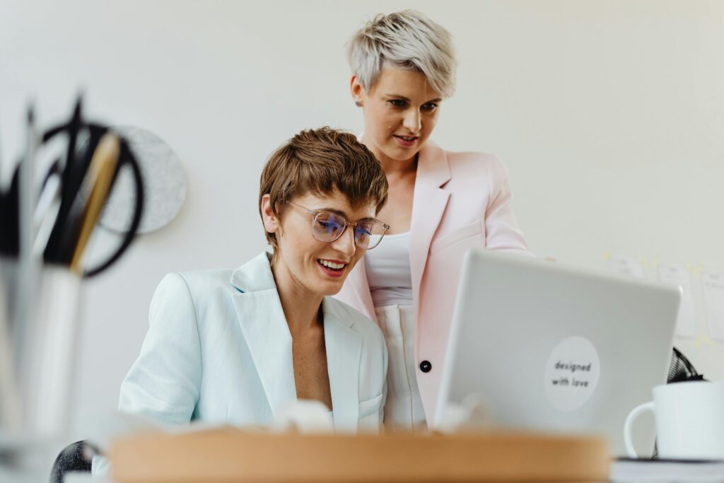 Two professional women working together happily on a laptop in a bright office setting.