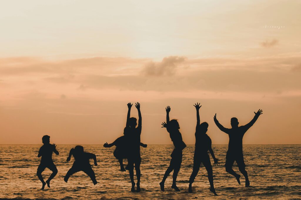Silhouettes of people jumping joyfully at the beach during sunset with an orange sky.