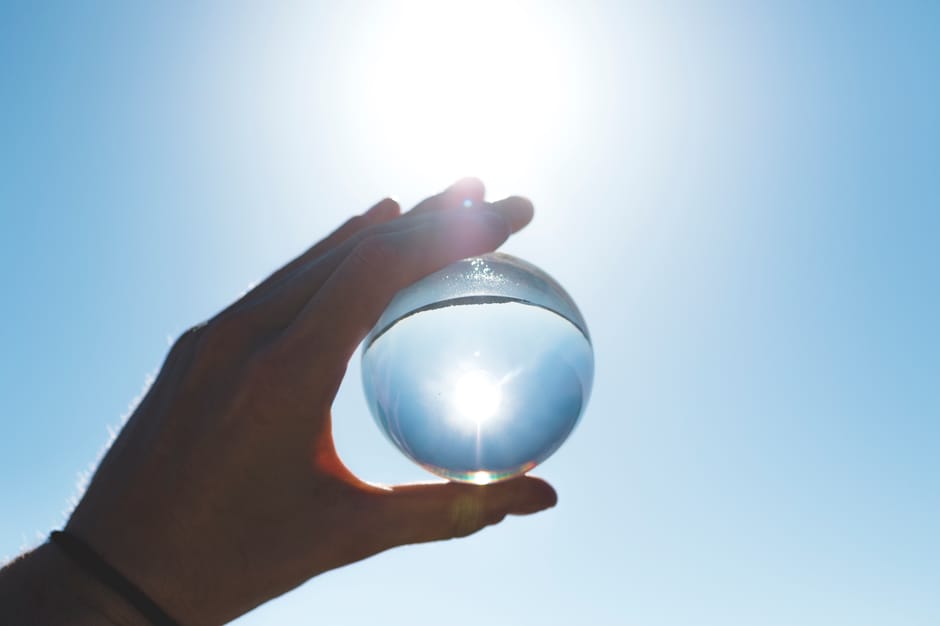 pexels-photo-1112196-1112196 A crystal ball held by a hand reflects the bright sun in a clear blue sky.