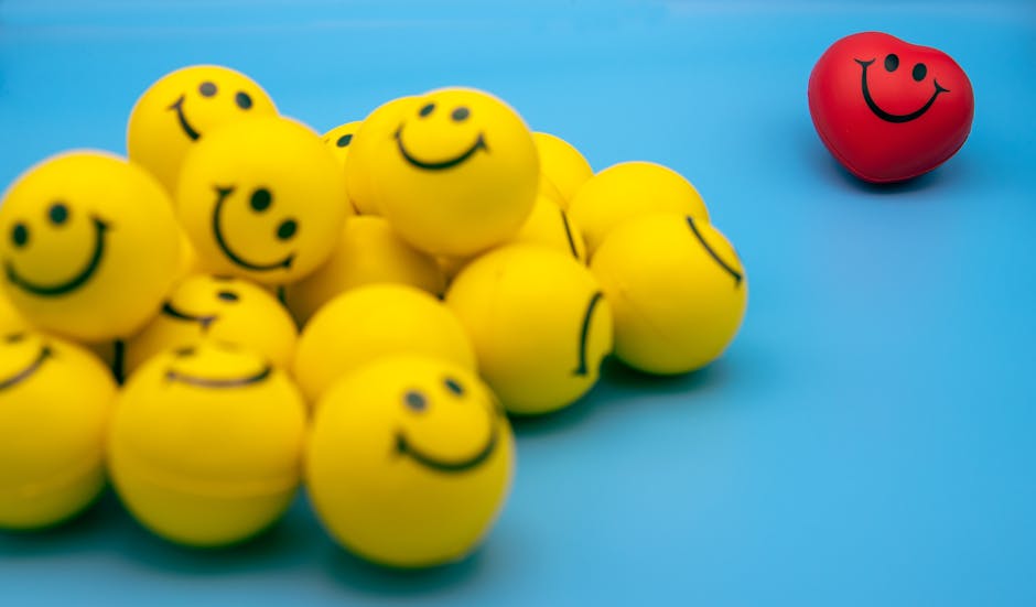 pexels-photo-8588945-8588945 A collection of yellow smiley balls with a red heart-shaped smiley on a blue background.