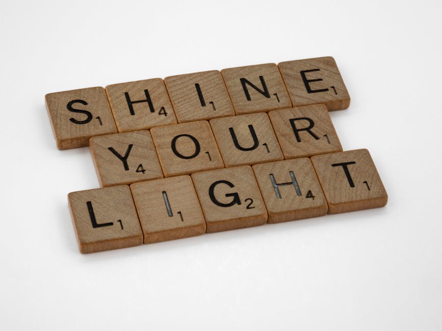 Close-up of wooden scrabble tiles spelling 'Shine Your Light' on a white surface.