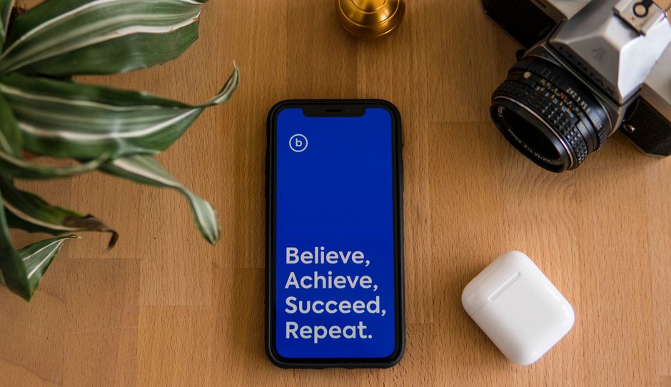 pexels-photo-9878734-9878734-1 Flat lay of smartphone displaying motivational text alongside camera and AirPods on a wooden surface.