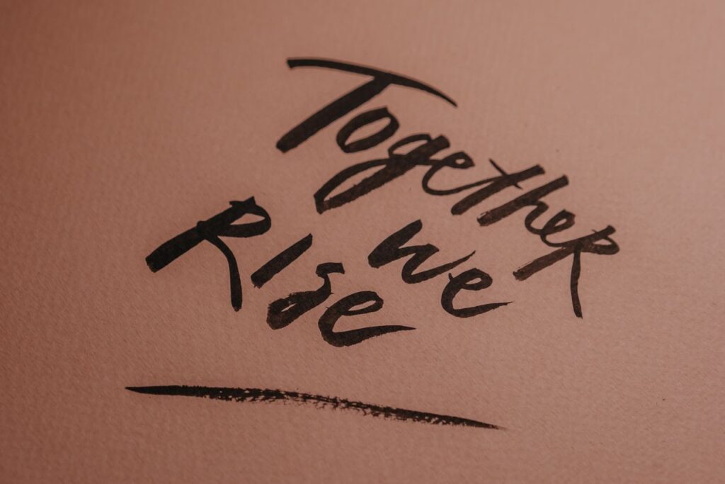 pexels-photo-6185558-6185558 Close-up of hand-lettered 'Together we Rise' on a textured pink background.